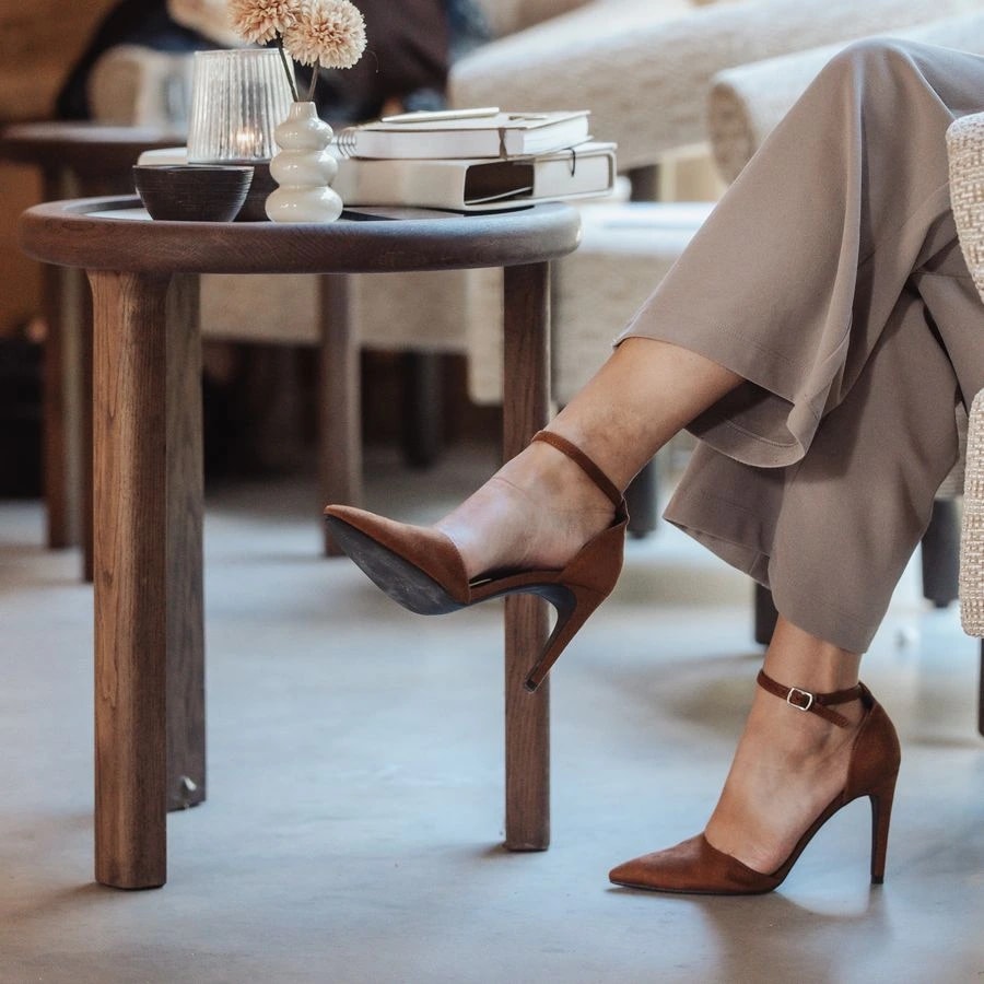 Detail van bruine pumps naast een houten tafel